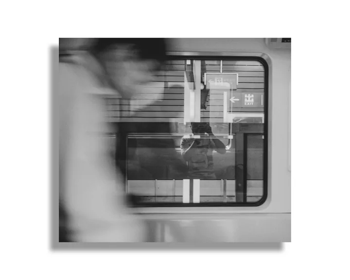 Black-and-white view through a train window with a blurred figure