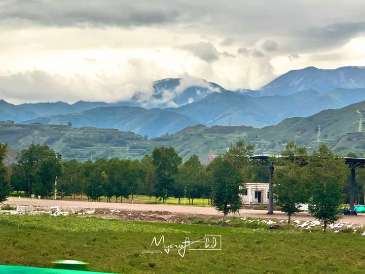 Fields and low buildings below cloud-covered mountains