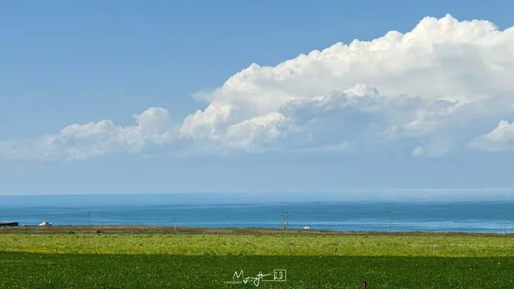 White clouds above blue water and a green field